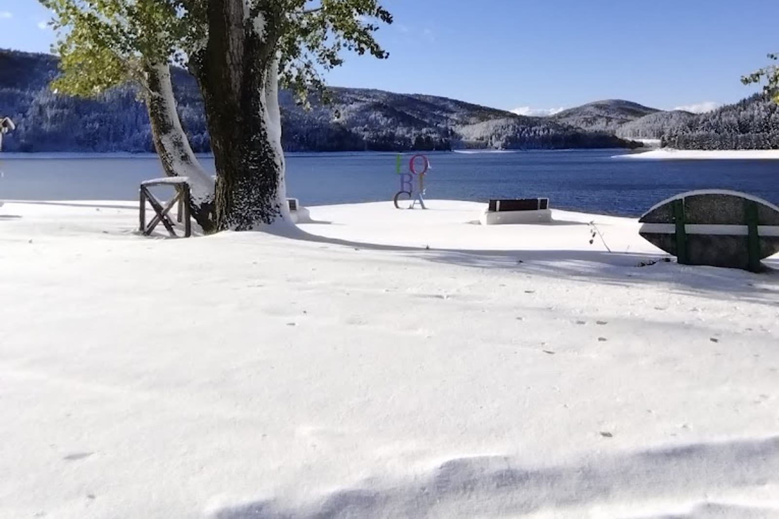 Winter view of Lorica with the colorful village sculpture overlooking the snow-covered Lake Arvo